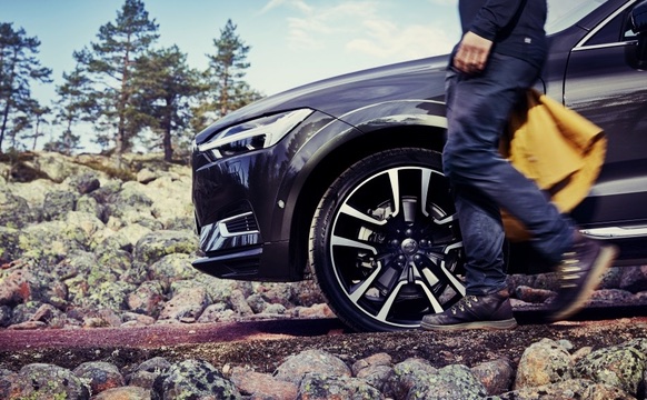 Vista lateral de rin frontal de modelo Volvo Sedán color negro en montaña, con conductor caminando a un lado
